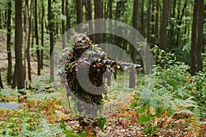 A highly skilled elite sniper, camouflaged in the dense forest, stealthily maneuvers through dangerous woodland terrain
