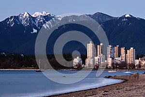 Highrise buildings by ocean and mountains at dusk.