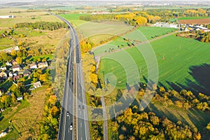 Highway between Autumn forest and cultivated ground with yellow trees at sunset in autumn. Aerial view of the traffic on speedway.