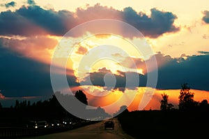 Highway with cars traveling on the sunset. Horizon line with the sun and storm clouds. Journeys. Selective focus