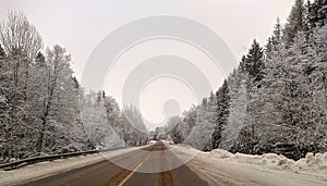 highway with horizon on blue sky and clouds in the daytime at winter with snow covered trees.