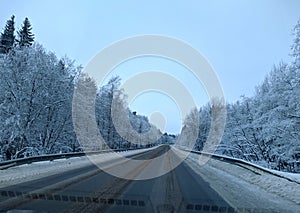 highway with horizon on blue sky and clouds in the daytime at winter with snow covered trees.
