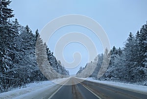 highway with horizon on blue sky and clouds in the daytime at winter with snow covered trees.