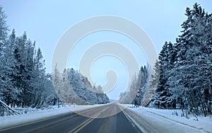 highway with horizon on blue sky and clouds in the daytime at winter with snow covered trees.