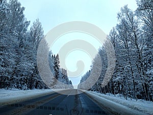 highway with horizon on blue sky and clouds in the daytime at winter with snow covered trees.