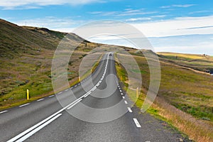 Highway through Icelandic landscape under a blue summer sky.