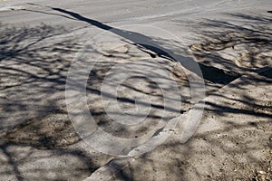 A highway with large pits and shadows from trees.