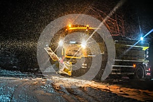 Highway maintenance truck cleaning road during heavy snowstorm in night, dangerous driving during winter transport calamity