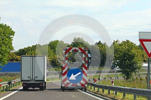 Highway maintenance truck with the road sign with the huge arrow to signal the narrowing of the roadway photo