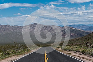 A highway receding to perspective toward a mountain range in a desert landscape
