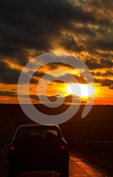 Highway road and car in front of orange sunset sky at winter