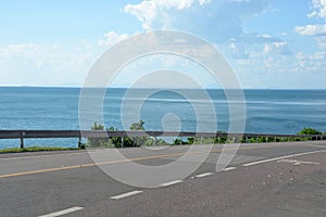 Highway road goes down in mountains with sea view in sunny day.