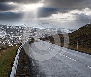 Highway road and mountain view with sun rays through clouds during auto trip in Iceland. Spectacular Icelandic landscape with