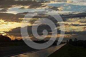 Highway traffic in sunset. Road with metal safety barrier. Cars on the asphalt under the cloudy sky.