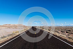 Highway vanishing to perspective on the horizon in a vast desert landscape under a bright blue sky