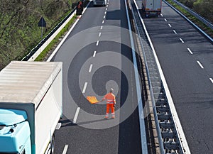 A highway worker with a high visibility work suit waves the orange flag to slow down traffic before the roadblock