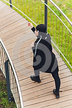 Hijab girl exercising on walkway bridge in early morning. Muslim woman wearing sports clothes doing stretching workout