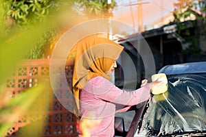 Hijab woman cleaning her car at outdoors. Transportation self service, care concept