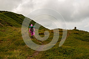 Hike backpacker lifestyle girl walking on trek trail in mountains outdoors with pink raincoat.