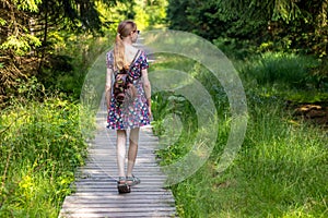 on a hike - a young woman in a summer dress walking on a wooden path in the forest