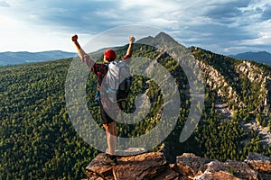 Hiker with arms up standing on the top of the mountain. A man with a backpack in the mountains at sunset, rear view.