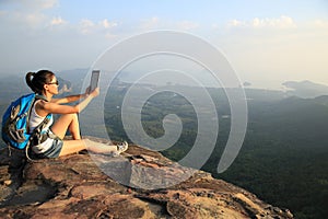 Hiker asian woman using digital tablet taking photo at mountain peak cliff