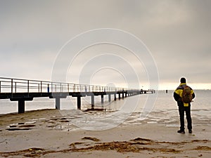 Hiker with backpack alone on sandy beach, sunrise above sea bridge.