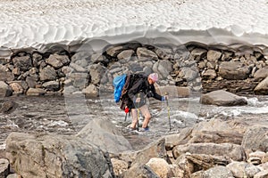 Hiker with backpack crosses cold creek. on a trekking tour in Sarek, Sweden, autumn, life style