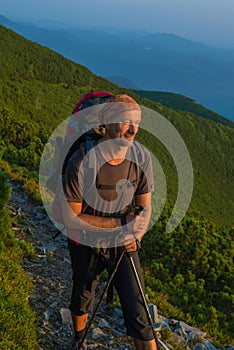 Hiker with backpack is resting and looks at the rising sun in mo