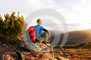 Hiker with backpack sitting on a rock by a tree against the background of dawn