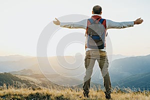 Hiker with backpack standing and rasing his hands at mountain ba