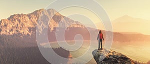 Hiker with a backpack on top of a rock admiring mountains view.