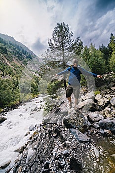 A hiker with backpack, a traveler, walks alone, balances stepping from boulder to stone. Caucasus mountains, The turbulent flow of