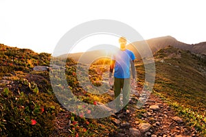 Hiker with backpack walking along a mountain trail in the background of dawn