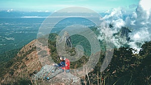 Hiker with backpacks reaches the summit of mountain peak. Female traveler on high top of rock enjoying wild environment landscape.