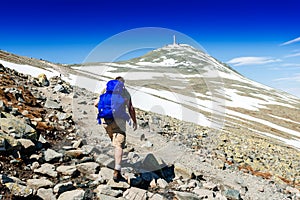 Hiker with big traveling rucksack looking forward on the mountain trail