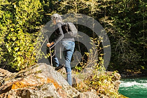 A hiker with a black backpack climbs to the top of a rock by the Skagit River