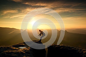 Hiker in black is jumping between mountains peaks.