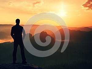 Hiker in black stand on the peak in rock empires park and watching over the misty and foggy morning valley to Sun. Beautiful mome