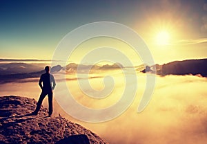 Hiker in black stands on rock abve valley within daybreak and watch to Sun. Beautiful moment the miracle of nature