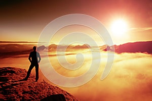 Hiker in black stands on rock abve valley within daybreak and watch to Sun. Beautiful moment the miracle of nature