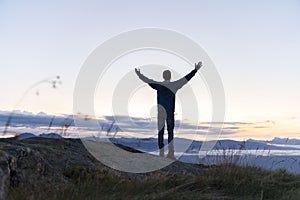 Hiker celebrating success on top of a mountain above the clouds. Young man enjoying freedome, Mountaineering sport lifestyle