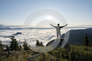 Hiker celebrating success on top of a mountain above the clouds. Young man enjoying freedome, Mountaineering sport lifestyle