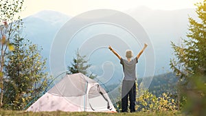 Hiker child boy resting near a tourist tent at mountain campsite enjoying view of beautiful summer nature.