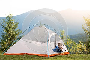 Hiker child boy resting sitting in a camping tent at mountains campsite enjoying view of summer nature