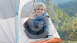 Hiker child boy resting sitting in a camping tent at mountains campsite enjoying view of summer nature.