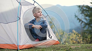Hiker child boy resting sitting in a camping tent at mountains campsite enjoying view of summer nature