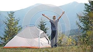 Hiker child boy resting standing near a camping tent at mountains campsite enjoying view of summer nature.