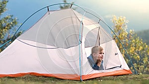 Hiker child boy resting in a tourist tent at mountain campsite enjoying view of beautiful summer nature.