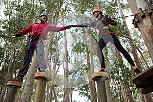 Hiker couple helping each other to cross obstacles in the forest